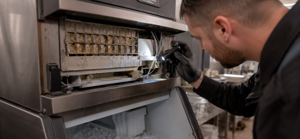 Commercial kitchen ice machine being inspected by a technician for contamination and food safety risks.
